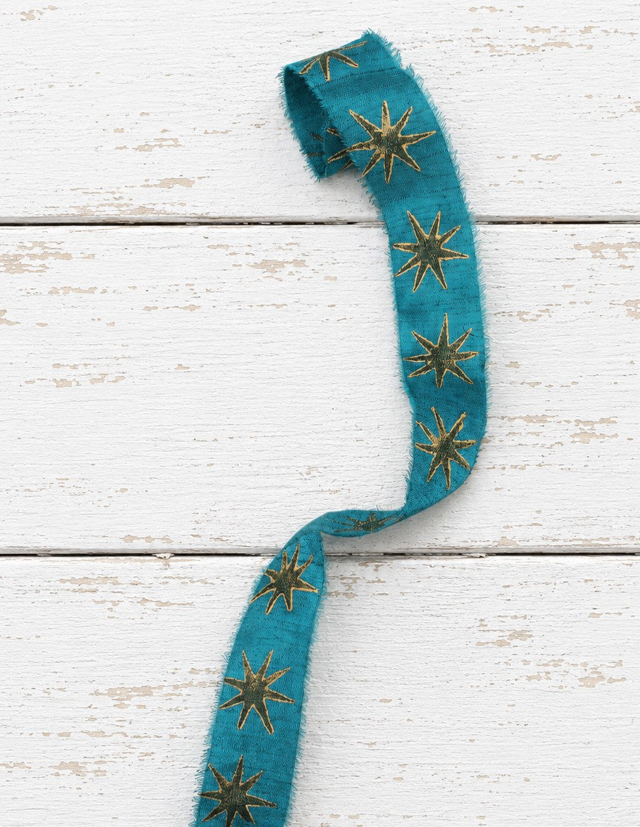 Teal block printed sari silk ribbon with gold star motif on white wooden background