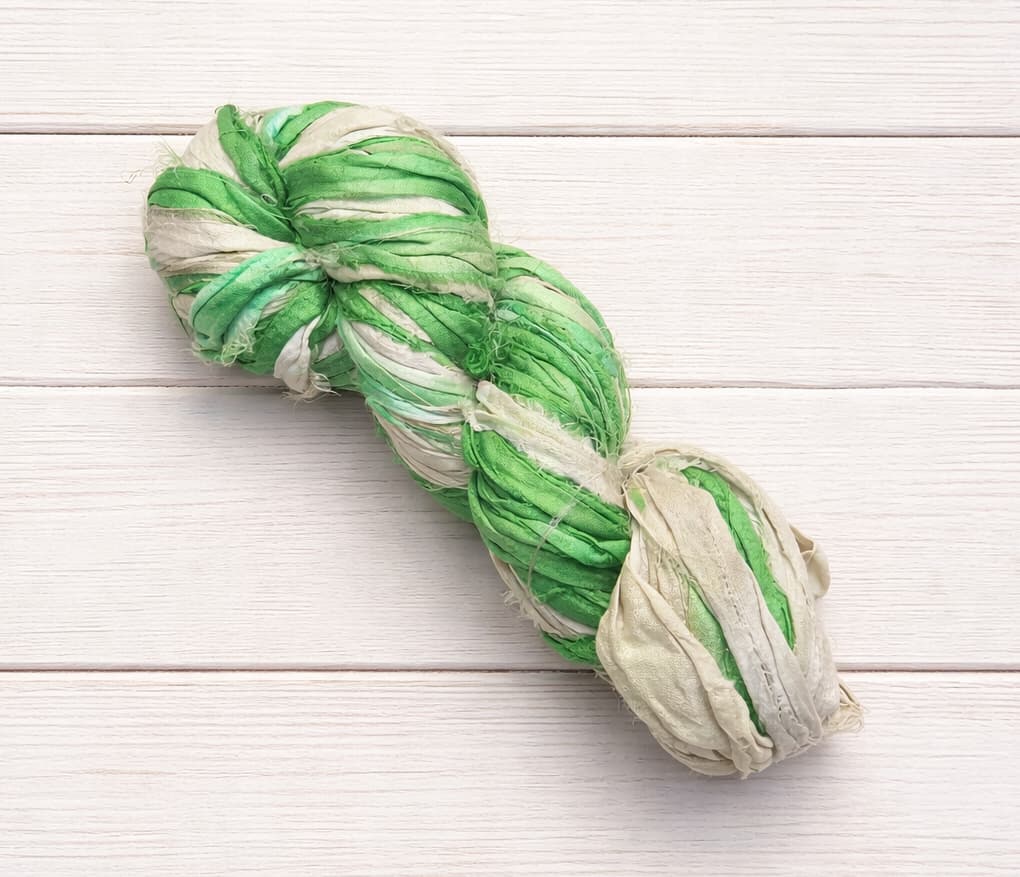 Variegated green and ivory sari silk ribbon yarn skein on white wood background