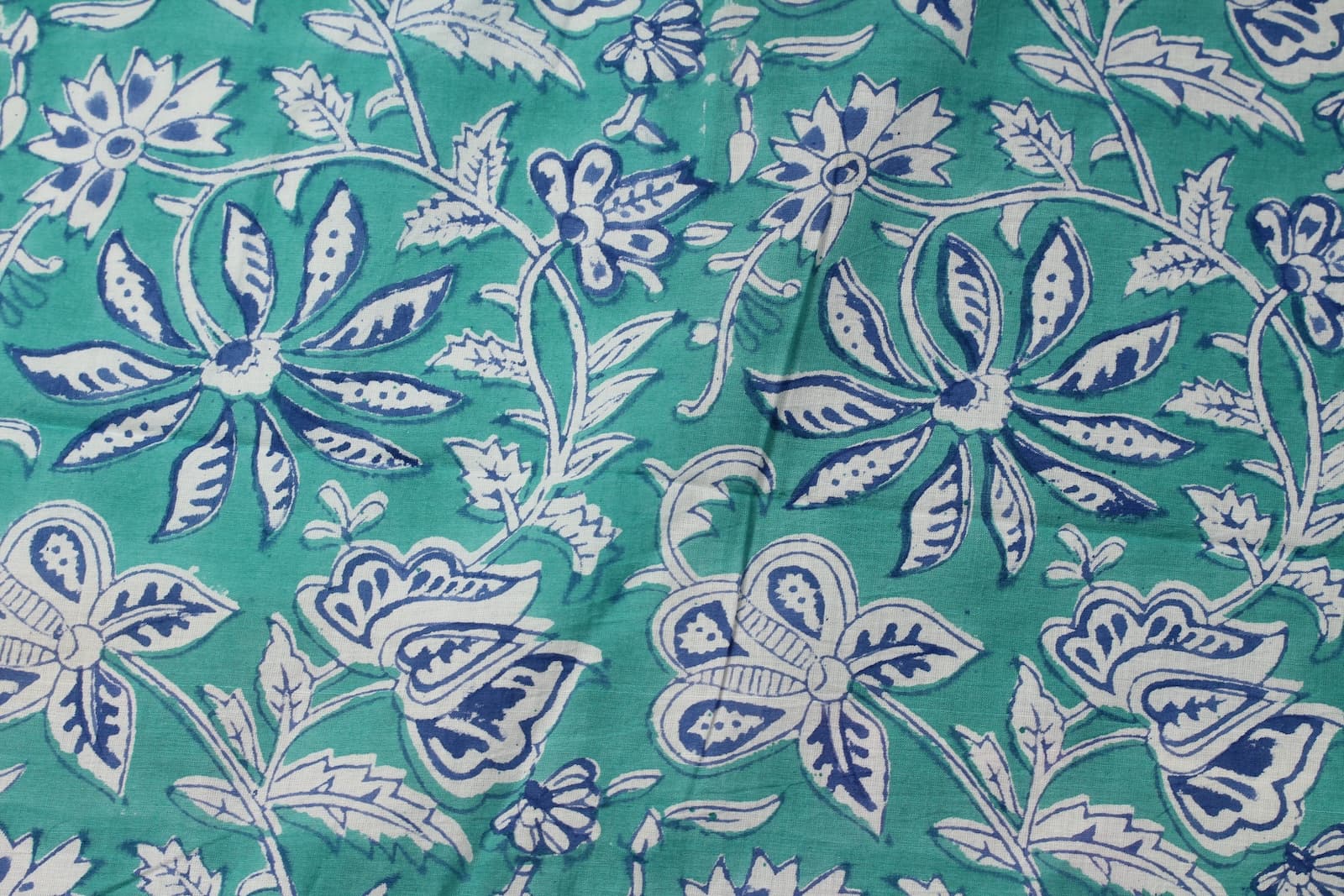 Close-up of turquoise floral block print cotton fabric featuring indigo blossoms, vines, and botanical motifs