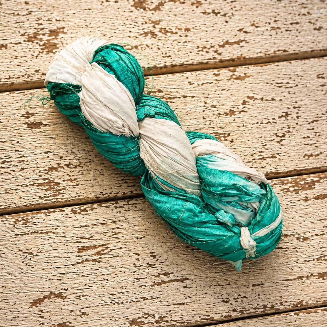 Seafoam and ivory sari silk ribbon yarn skein photographed on rustic wood background