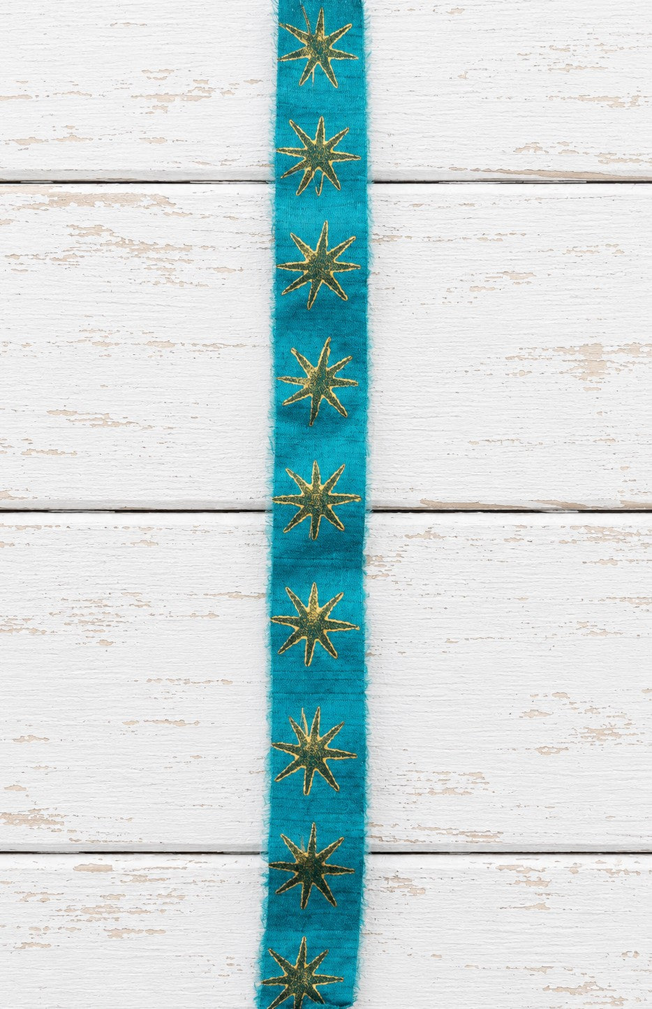 Close-up of teal block printed silk ribbon with repeating gold star pattern