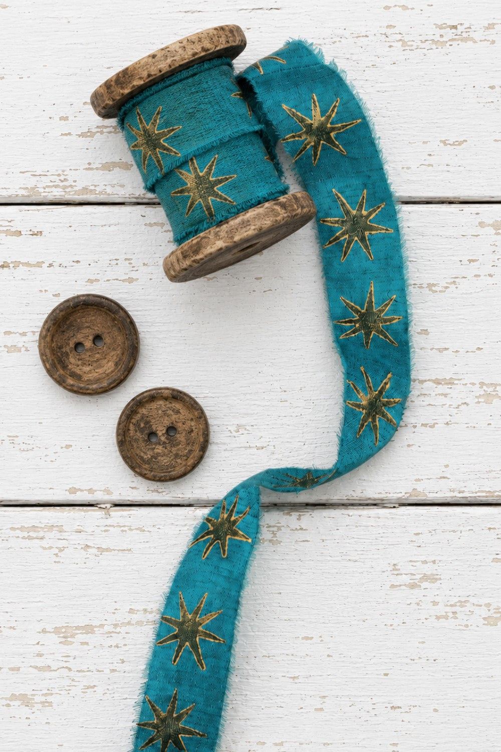 Teal block printed silk ribbon with gold star pattern displayed on wooden spool