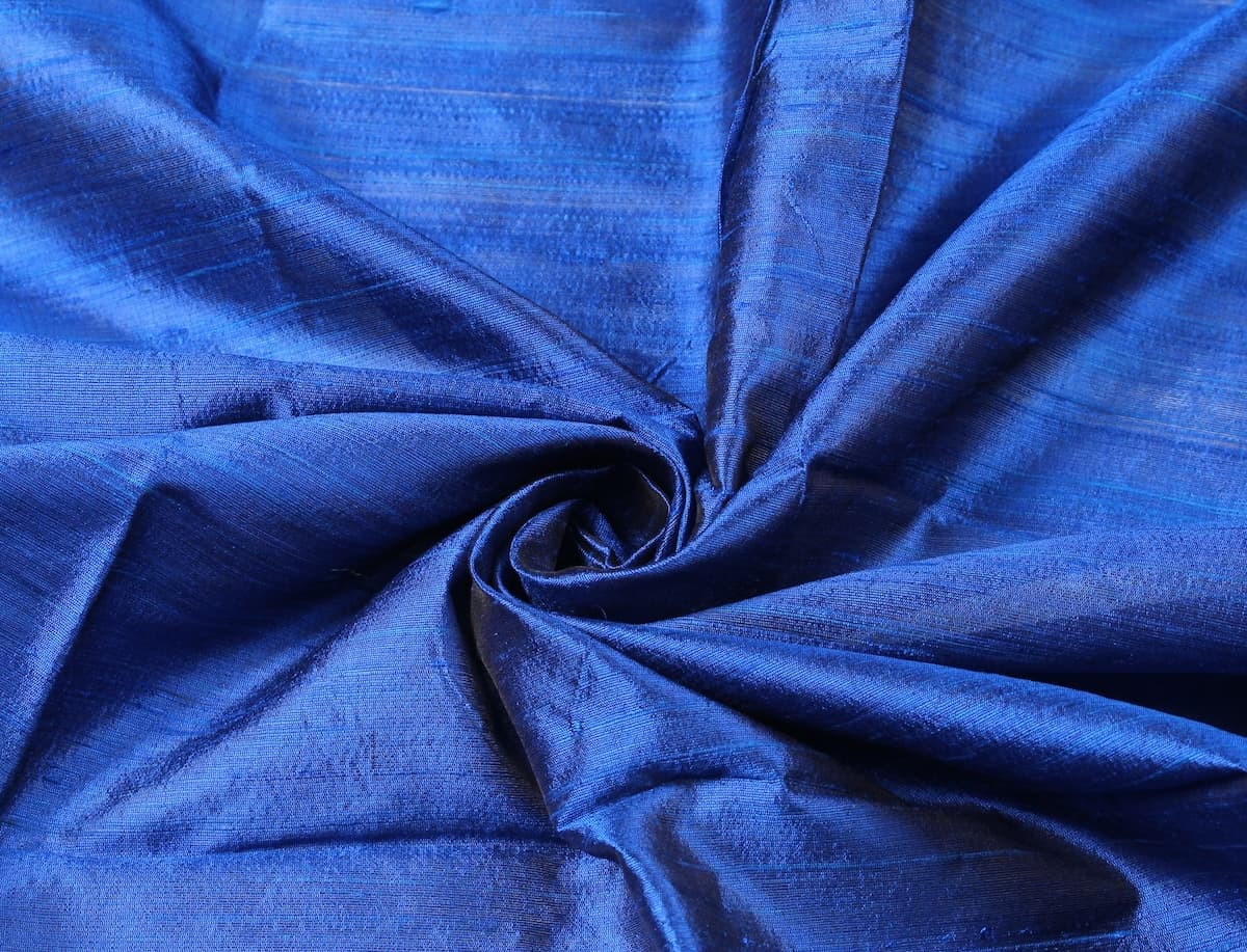 Royal Blue Dupion Silk Fabric arranged in elegant swirling folds highlighting its luminous sheen, crisp texture, and rich blue tones
