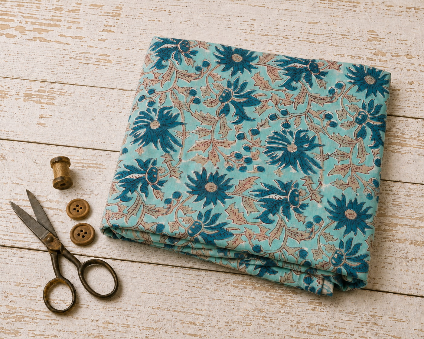 Folded aqua hand block printed cotton fabric featuring blue floral blooms and trailing botanical vines