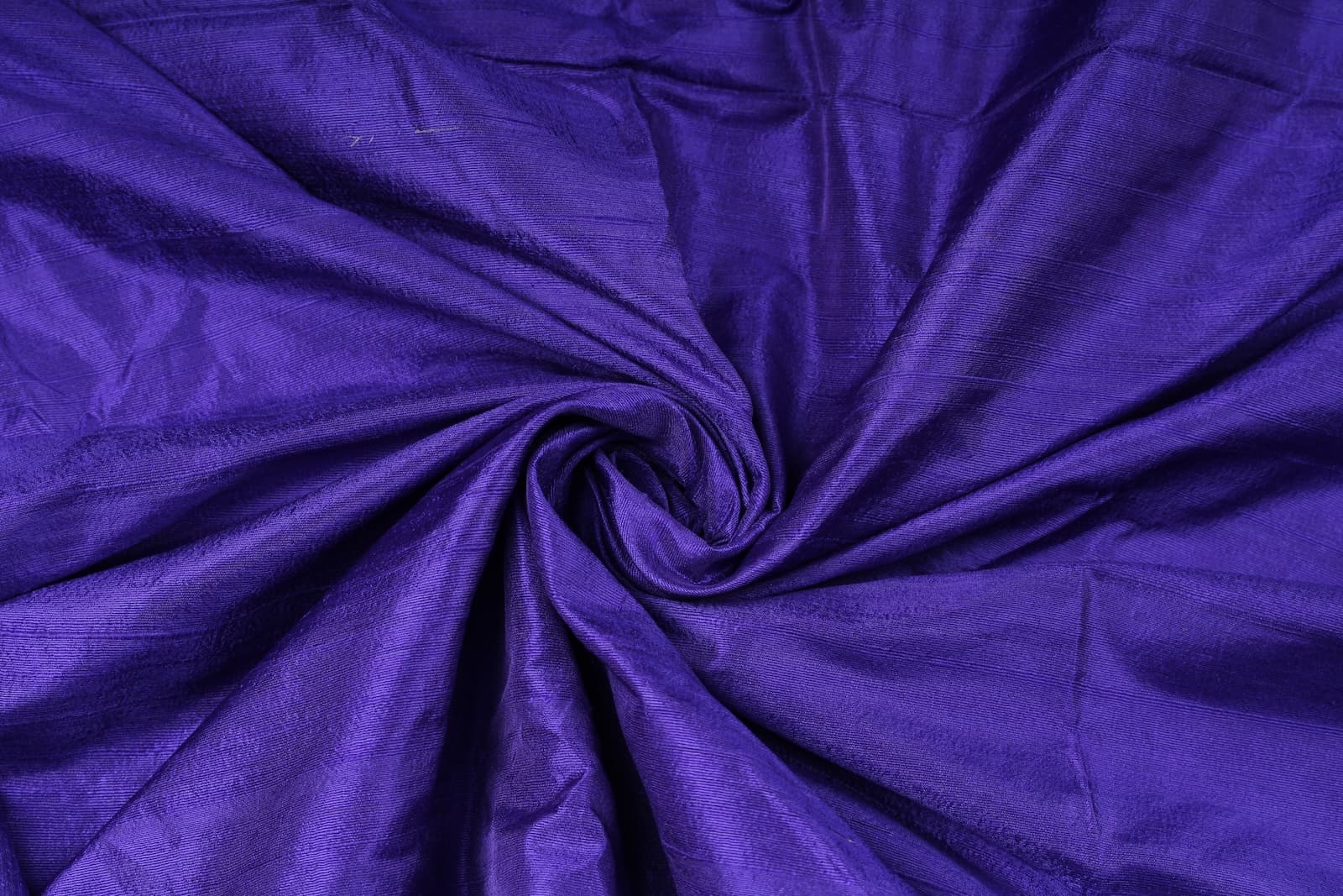 Blue Violet Dupion Silk Fabric arranged in elegant swirling folds highlighting its lustrous sheen, crisp texture, and rich jewel-toned colouring