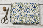 Hand block printed cotton fabric with blue floral blooms and green foliage on an ivory background