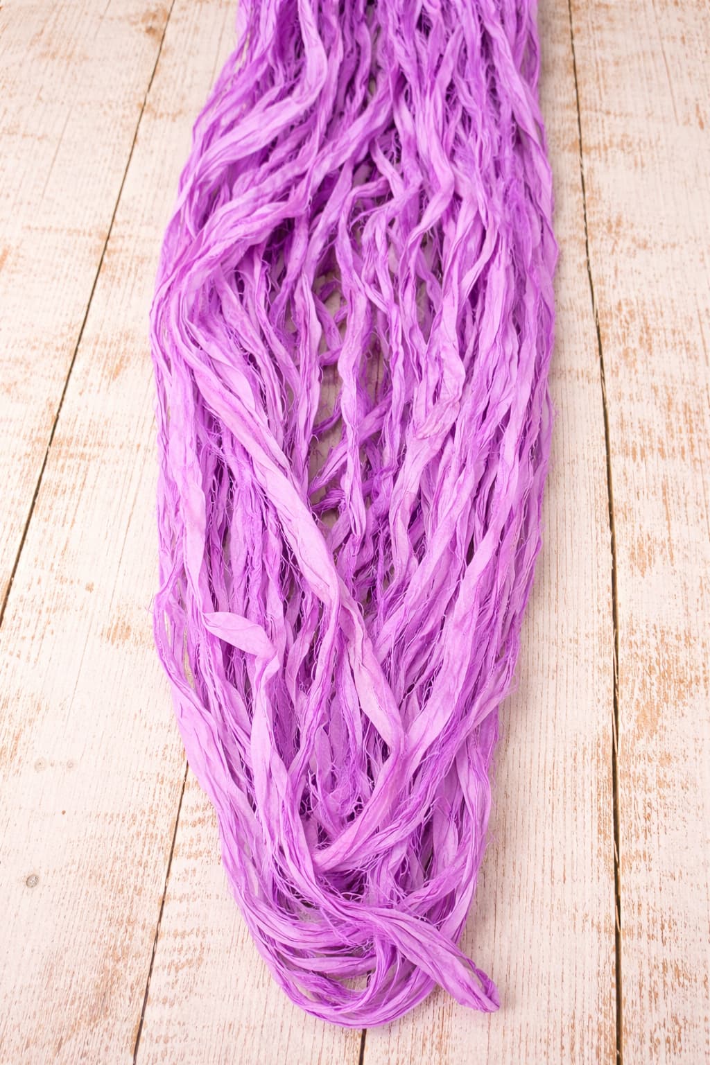 Orchid sari silk ribbon in loose strands showing soft texture and naturally frayed edges.