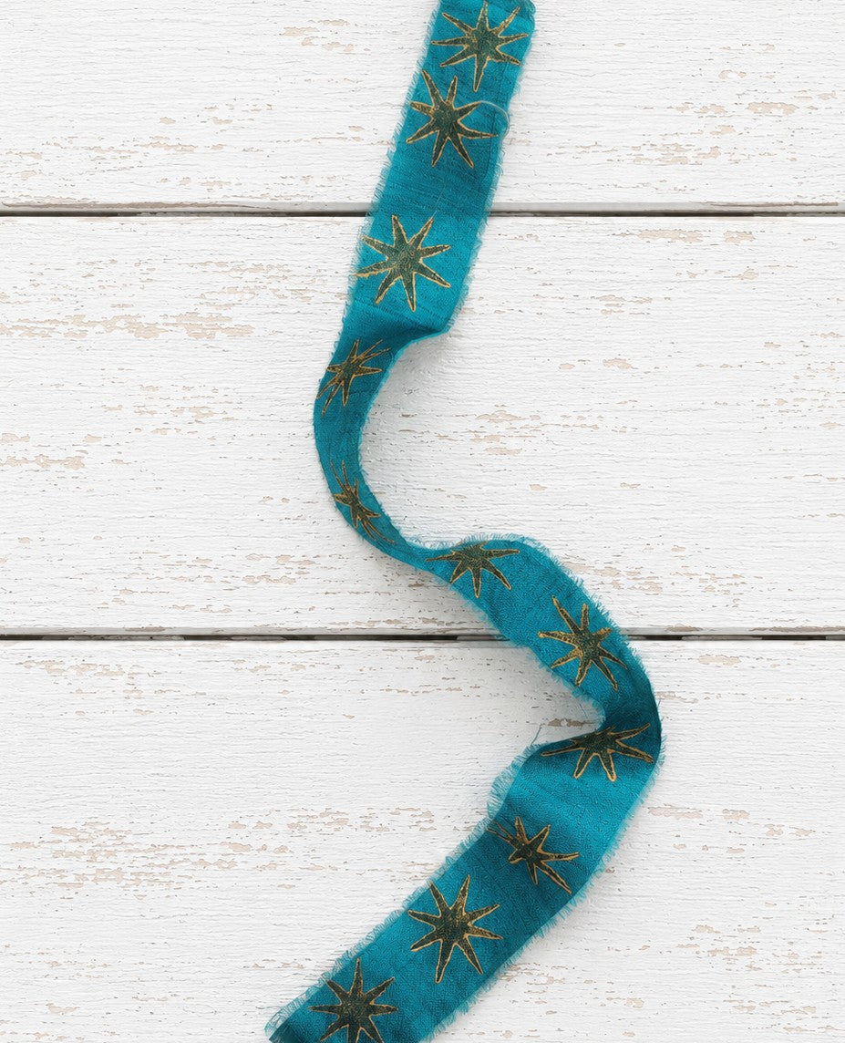 Hand block printed teal silk ribbon featuring gold stars on rustic white wood