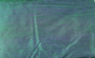 Close-up of Peacock Lagoon dupion silk fabric showing peacock blue and emerald green colour shifts with natural raw silk texture and slubs