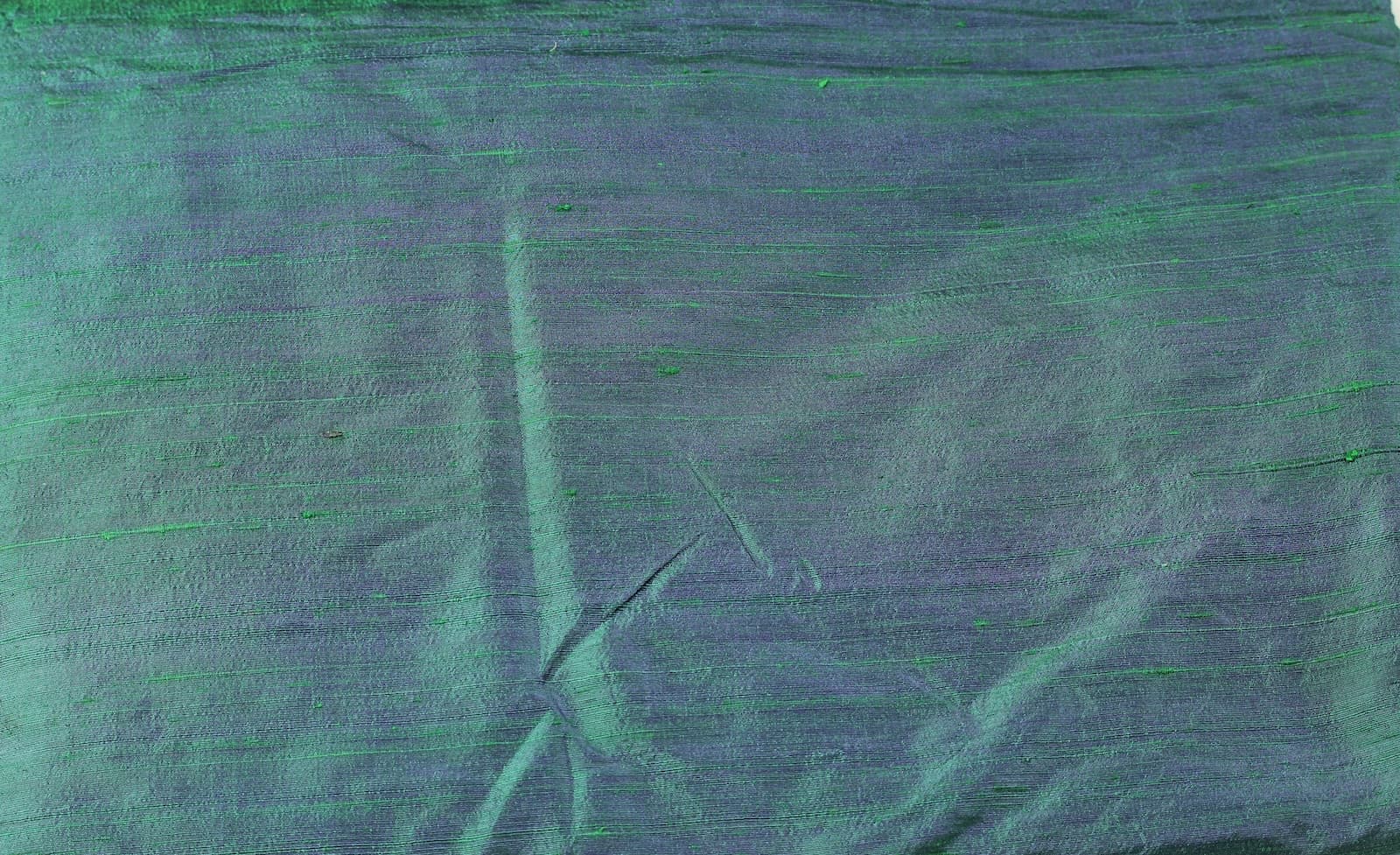 Close-up of Peacock Lagoon dupion silk fabric showing peacock blue and emerald green colour shifts with natural raw silk texture and slubs