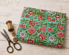 Coral Wildflower Meadow block printed cotton fabric folded on a white wooden surface with vintage scissors and thread spool