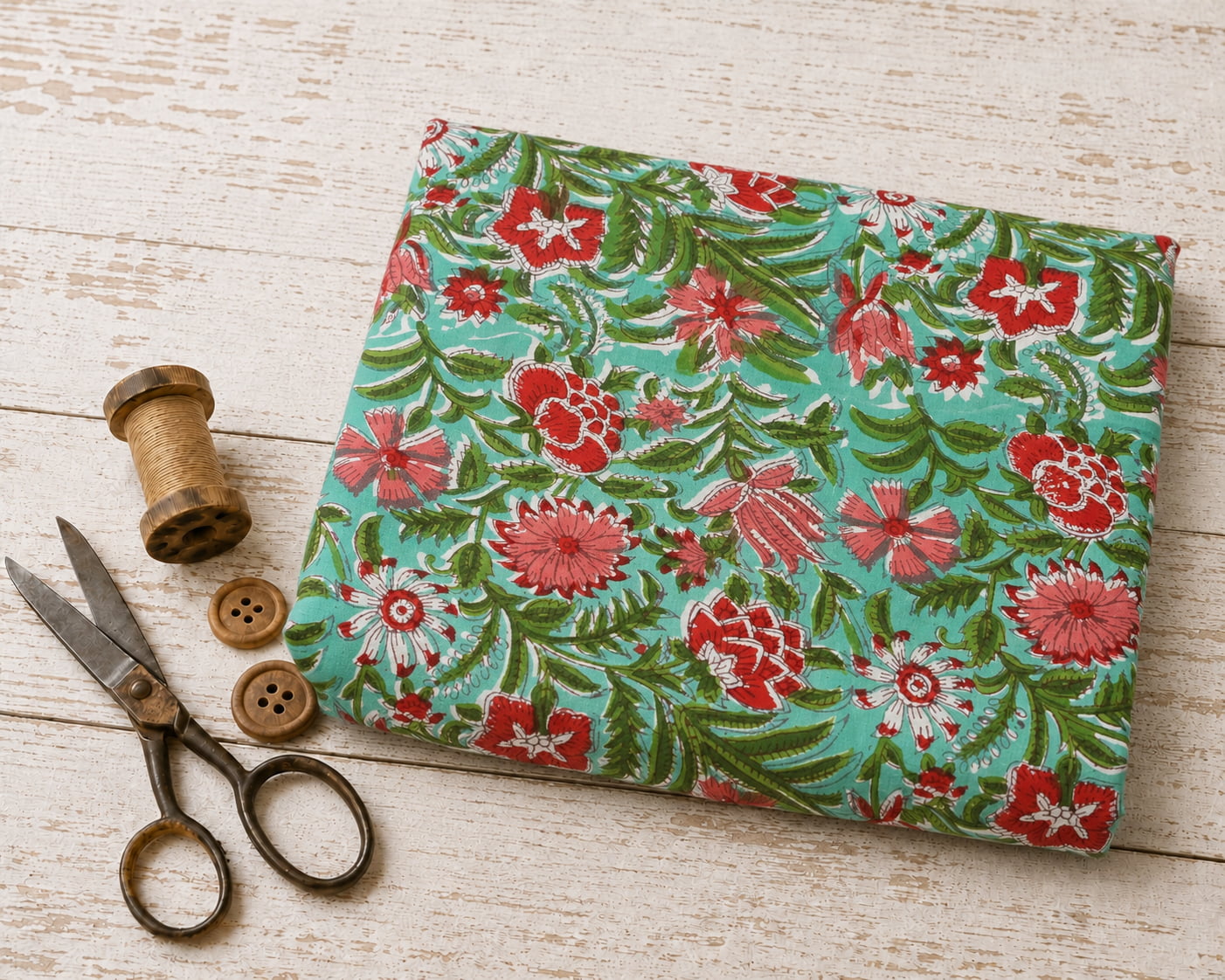 Coral Wildflower Meadow block printed cotton fabric folded on a white wooden surface with vintage scissors and thread spool