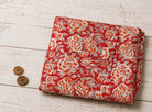 Crimson Rosewood block printed cotton fabric folded on a wooden surface with vintage sewing accessories