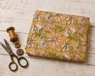 Folded golden mustard hand block printed cotton fabric with pink floral blossoms and green vine motifs