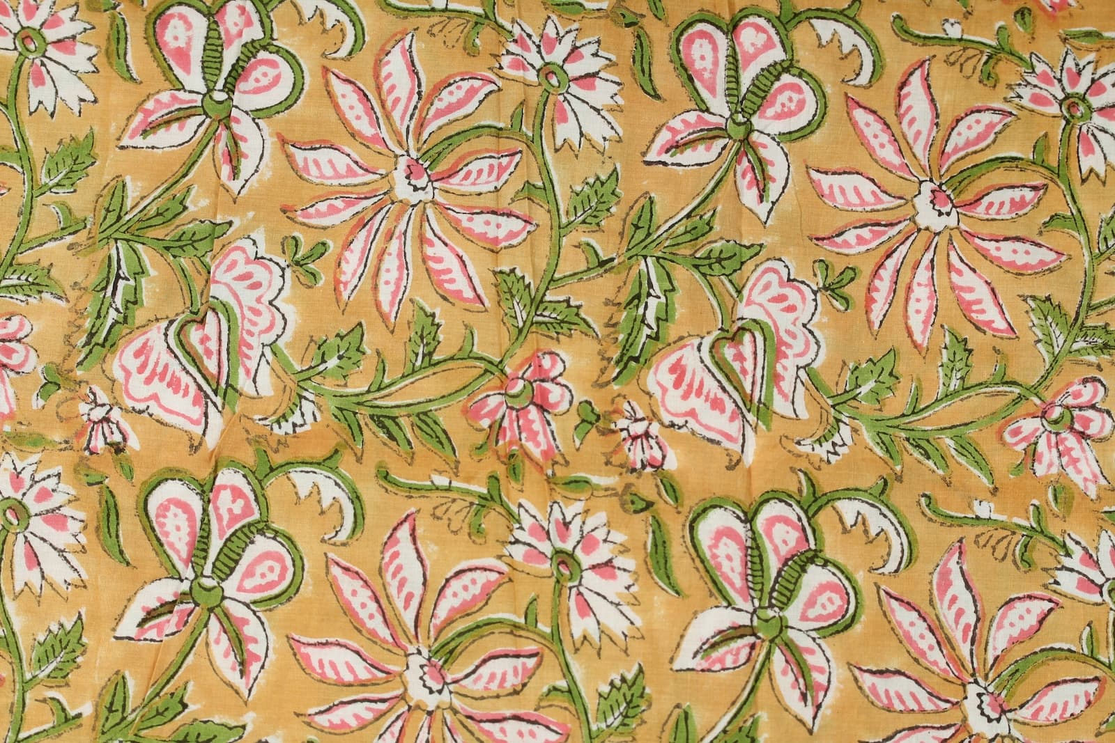 Close-up of pink jasmine-inspired floral motifs and leafy vines on golden hand block printed cotton fabric