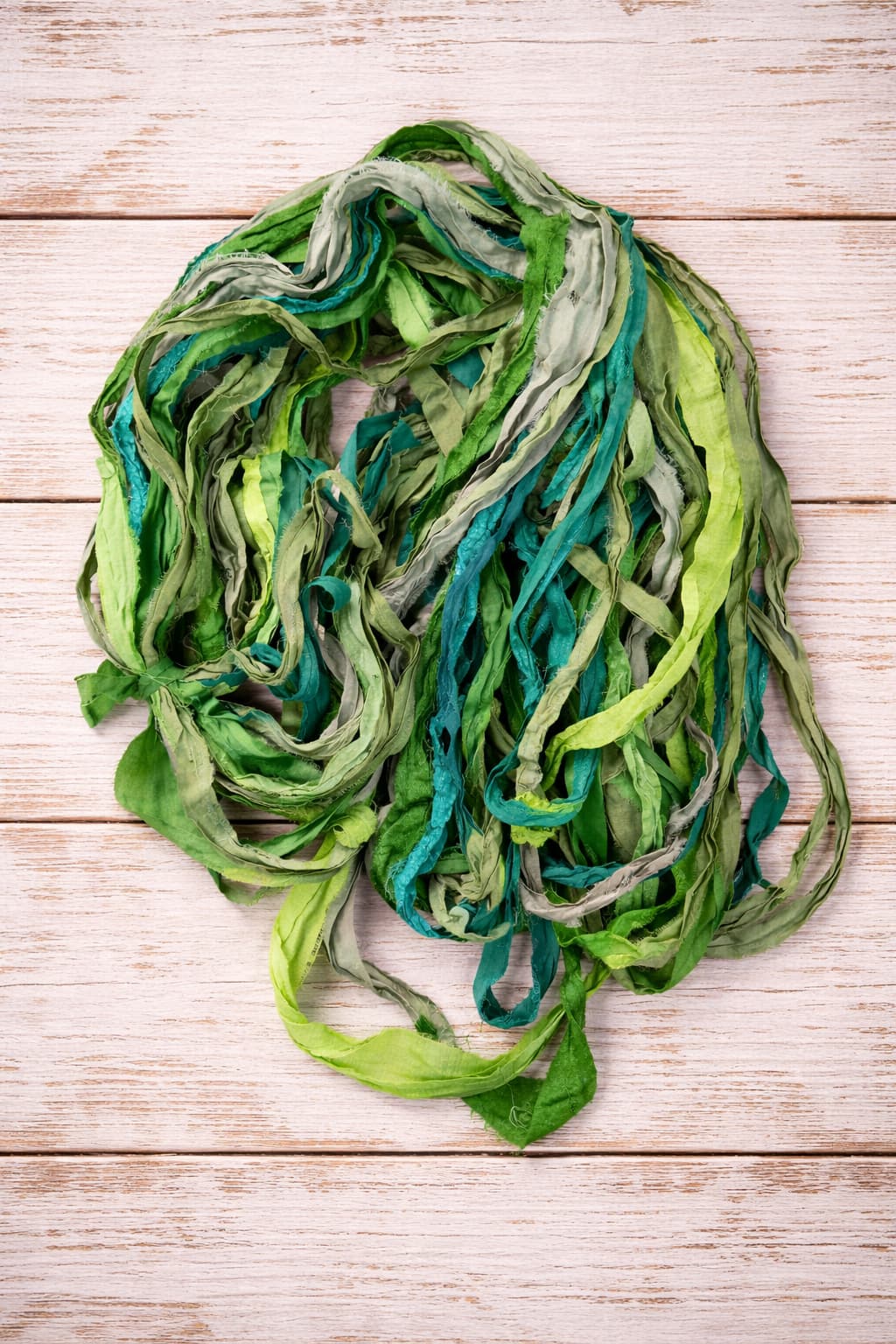 Loose bundle of Emerald Meadow sari silk ribbon yarn showing mixed green tones