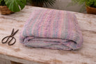 Handwoven sari ribbon fabric in pastel pink and lilac tones folded on a rustic wooden table.