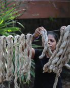 Woman hanging natural nettle fibers to dry outdoors — traditional preparation of plant fiber used in yarn.