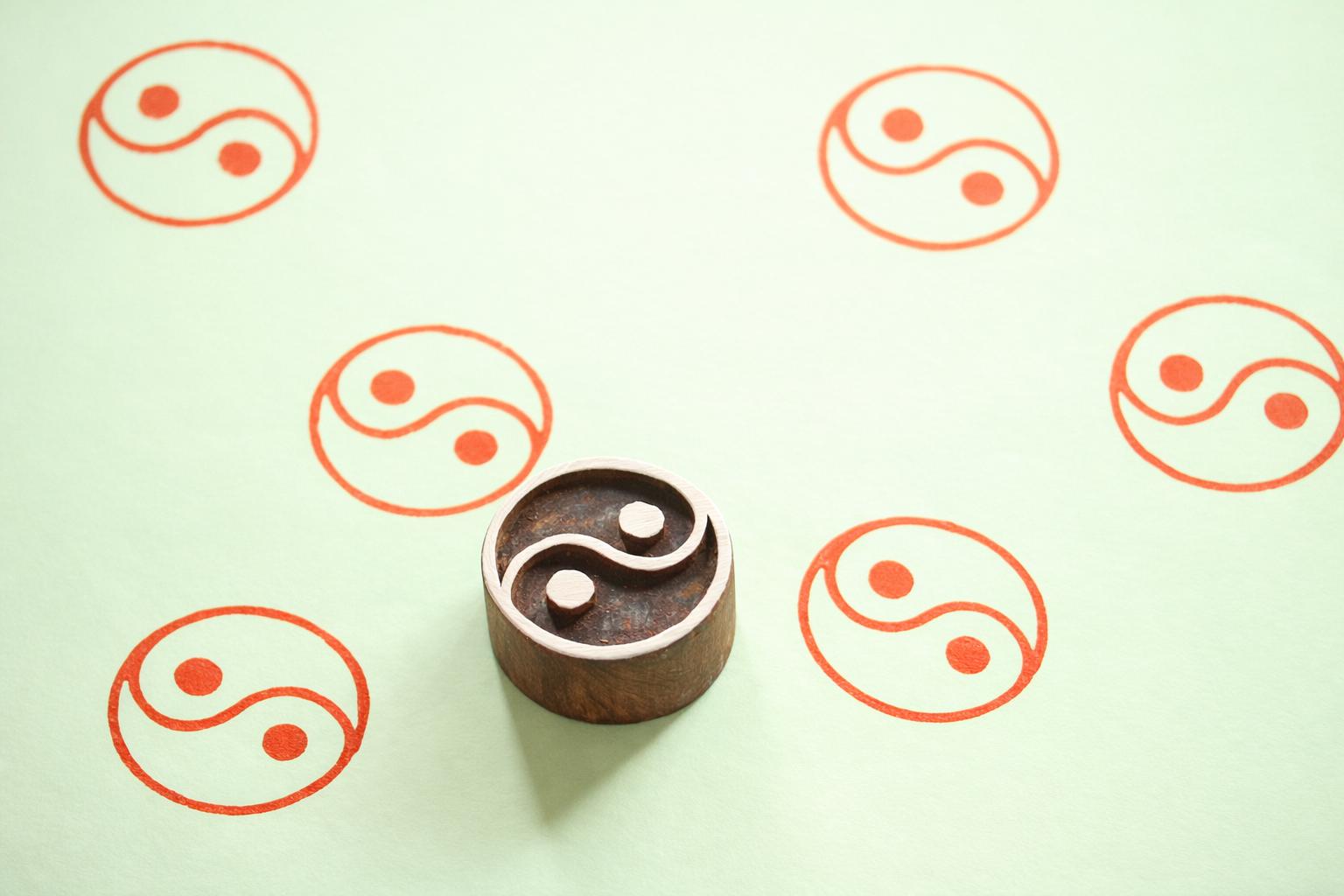 Hand carved yin yang wooden printing block with balance symbol stamped on soft green background