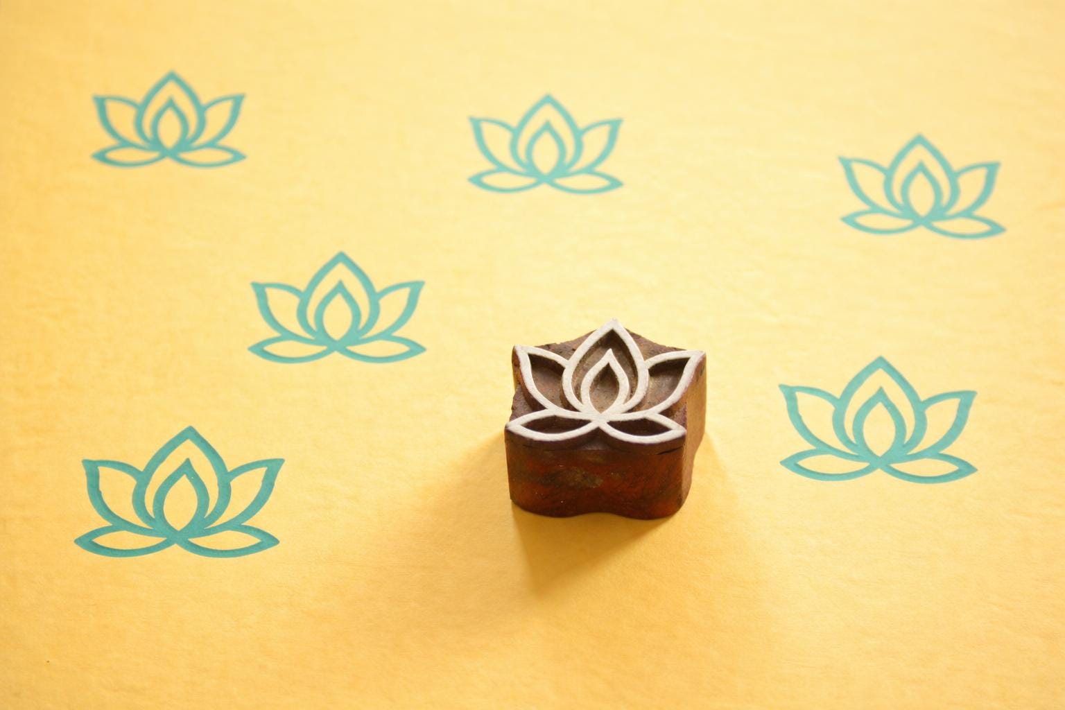 Hand carved lotus flower wooden printing block shown with repeated lotus prints on yellow background