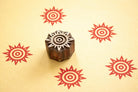 Hand carved Indian wooden printing block with a sunburst symbol shown on yellow fabric with repeated red sunburst prints.