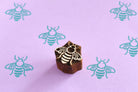 Hand carved bee wooden printing block shown with repeated bee prints on pastel purple paper