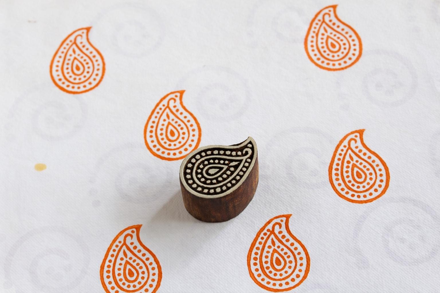 Hand carved paisley wooden printing block stamping orange paisley patterns on white fabric.