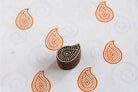Hand carved paisley wooden printing block stamping orange paisley patterns on white fabric.