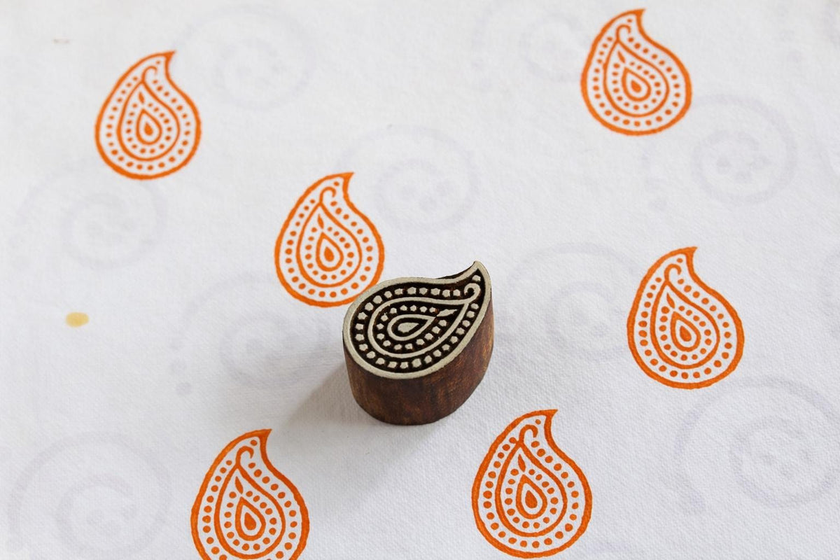Hand carved paisley wooden printing block stamping orange paisley patterns on white fabric.