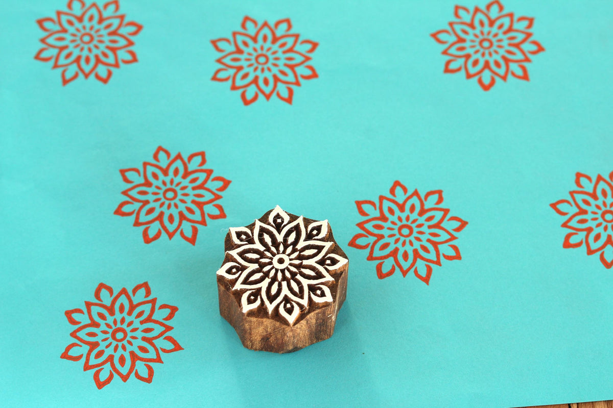 Large hand carved mandala wooden printing block on turquoise background with red floral repeat impressions.