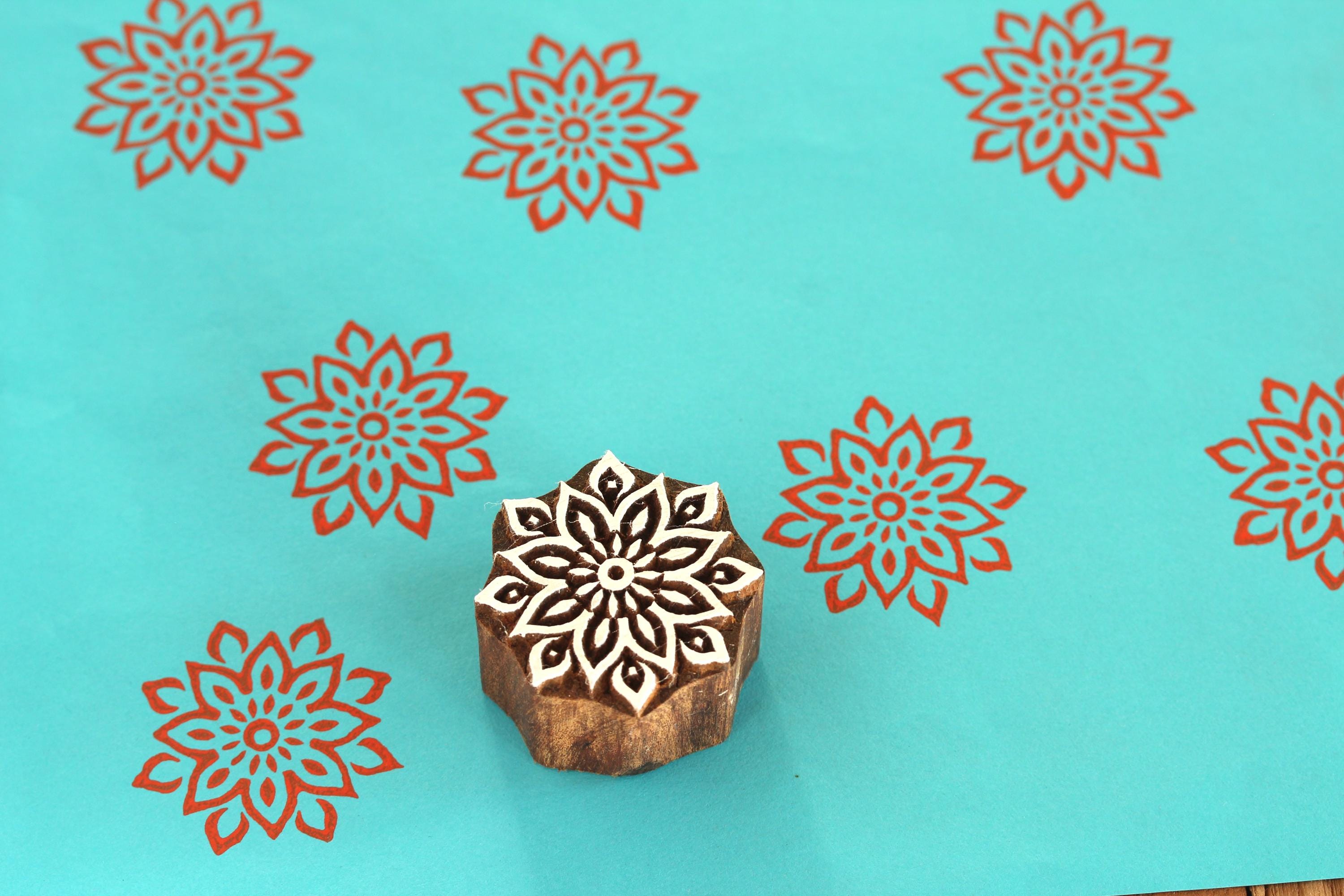 Large hand carved mandala wooden printing block on turquoise background with red floral repeat impressions.