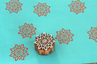Large hand carved mandala wooden printing block on turquoise background with red floral repeat impressions.
