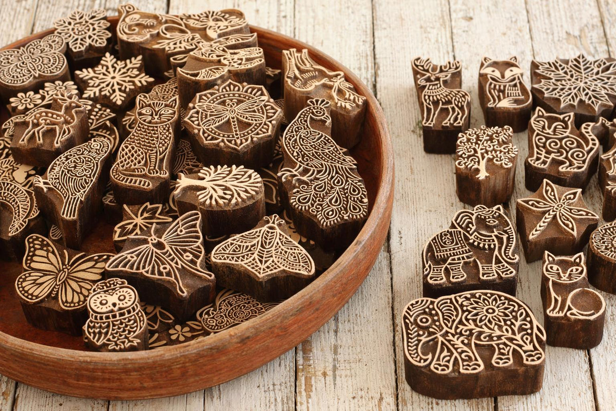 Assorted hand carved wooden printing blocks including animals, florals and nature designs arranged in a wooden tray for custom bundle offer.