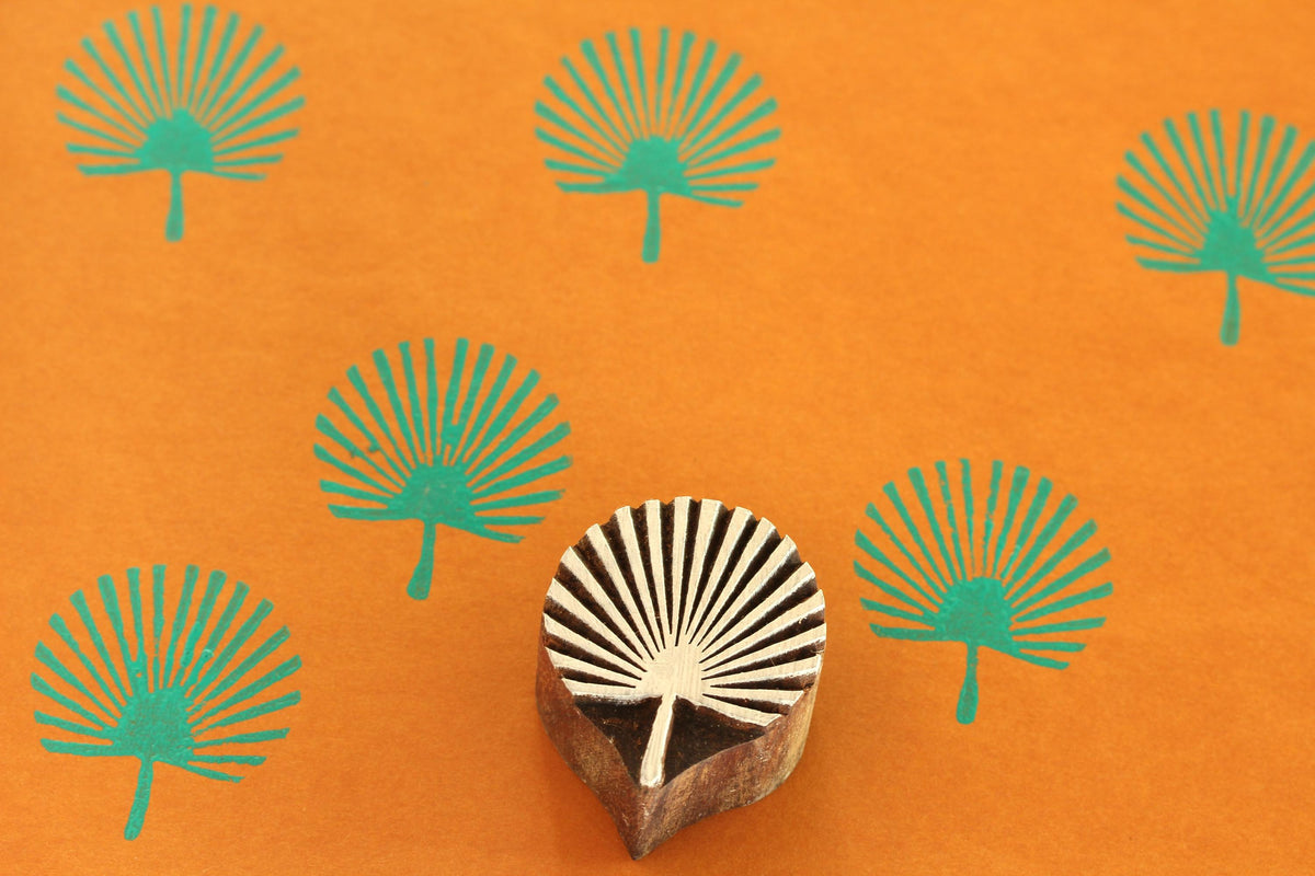 Hand carved palm fan wooden printing block with teal printed pattern on orange background.