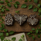 Hand carved wooden printing block set with bee dragonfly and ladybug designs displayed on rustic wood with green leaves