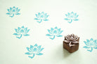 Small wooden lotus block printing stamp with repeating blue lotus pattern on mint green paper.
