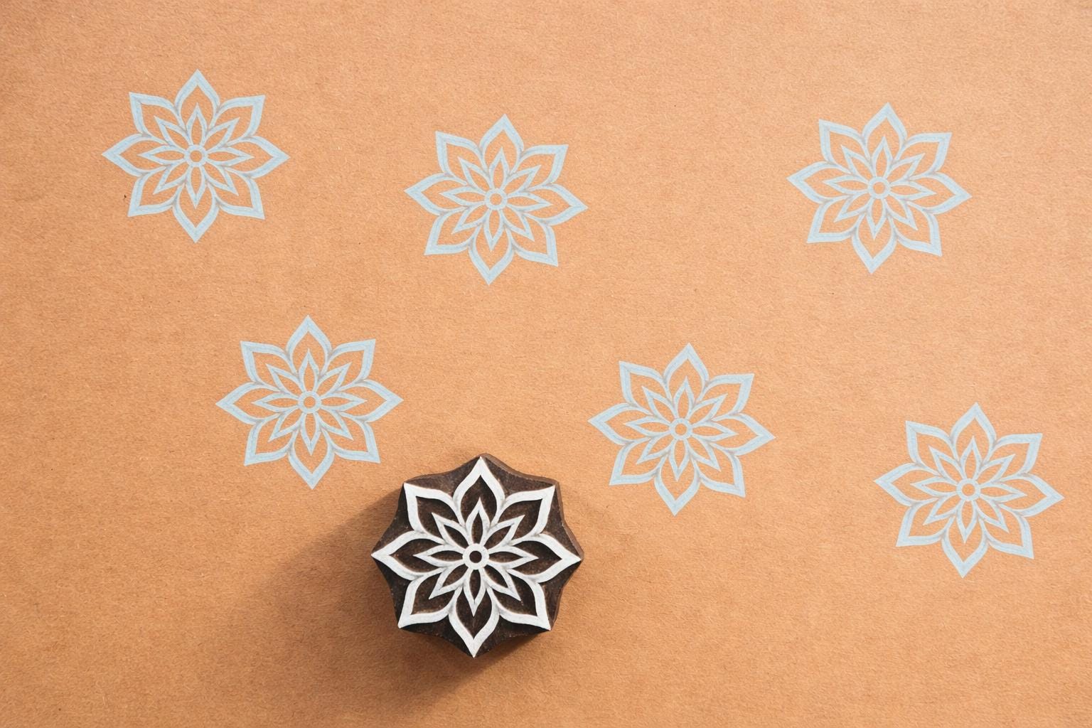 Hand carved wooden floral medallion block printing stamp creating repeating geometric flower pattern.