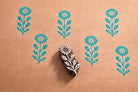 Hand carved wooden wildflower block printing stamp creating repeating floral pattern on kraft paper.