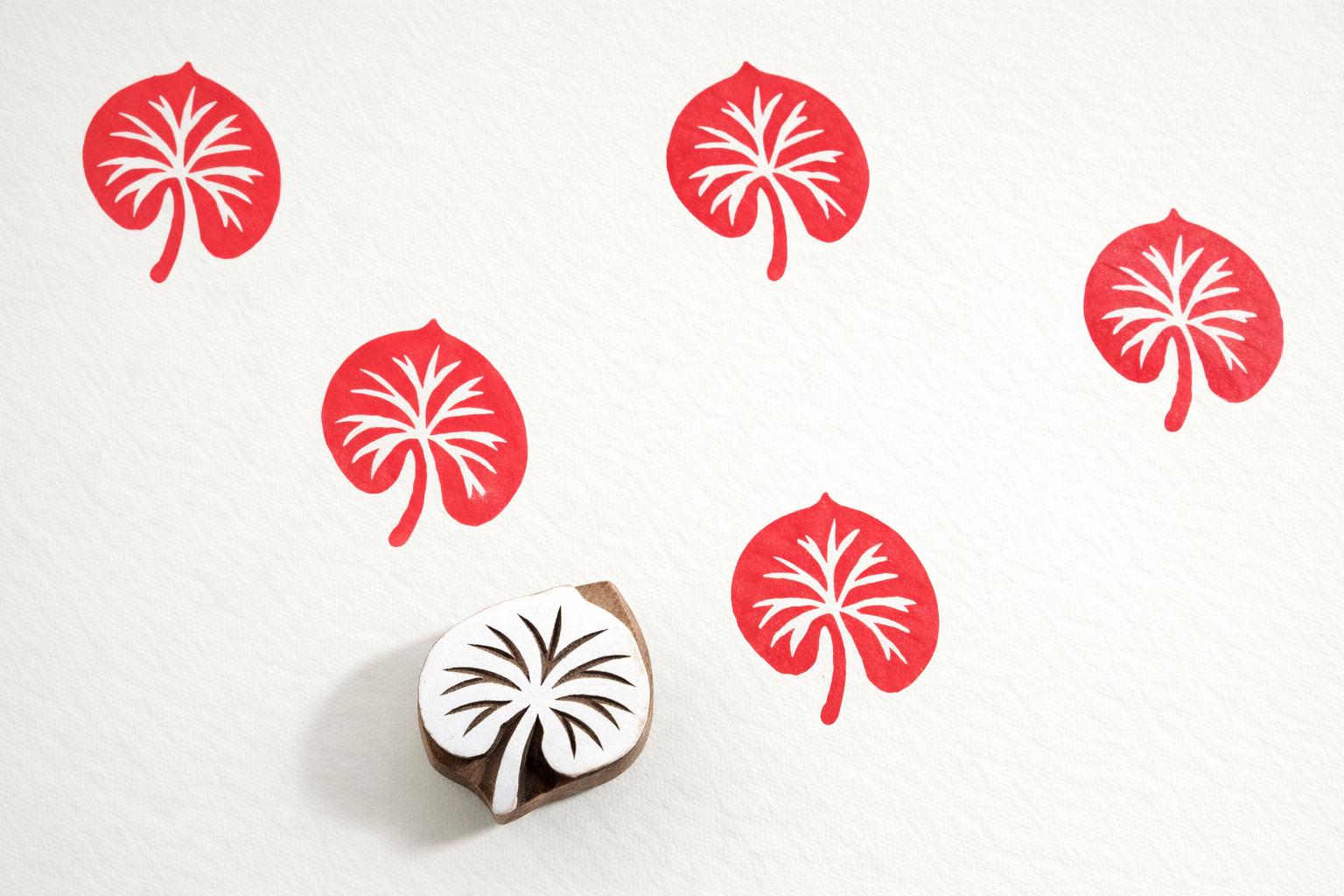 Round lily pad wooden block printing stamp creating repeating red botanical pattern on white fabric.