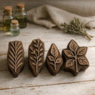Set of four hand carved wooden botanical leaf block printing stamps styled on rustic wood table with herbal bottles and linen fabric.