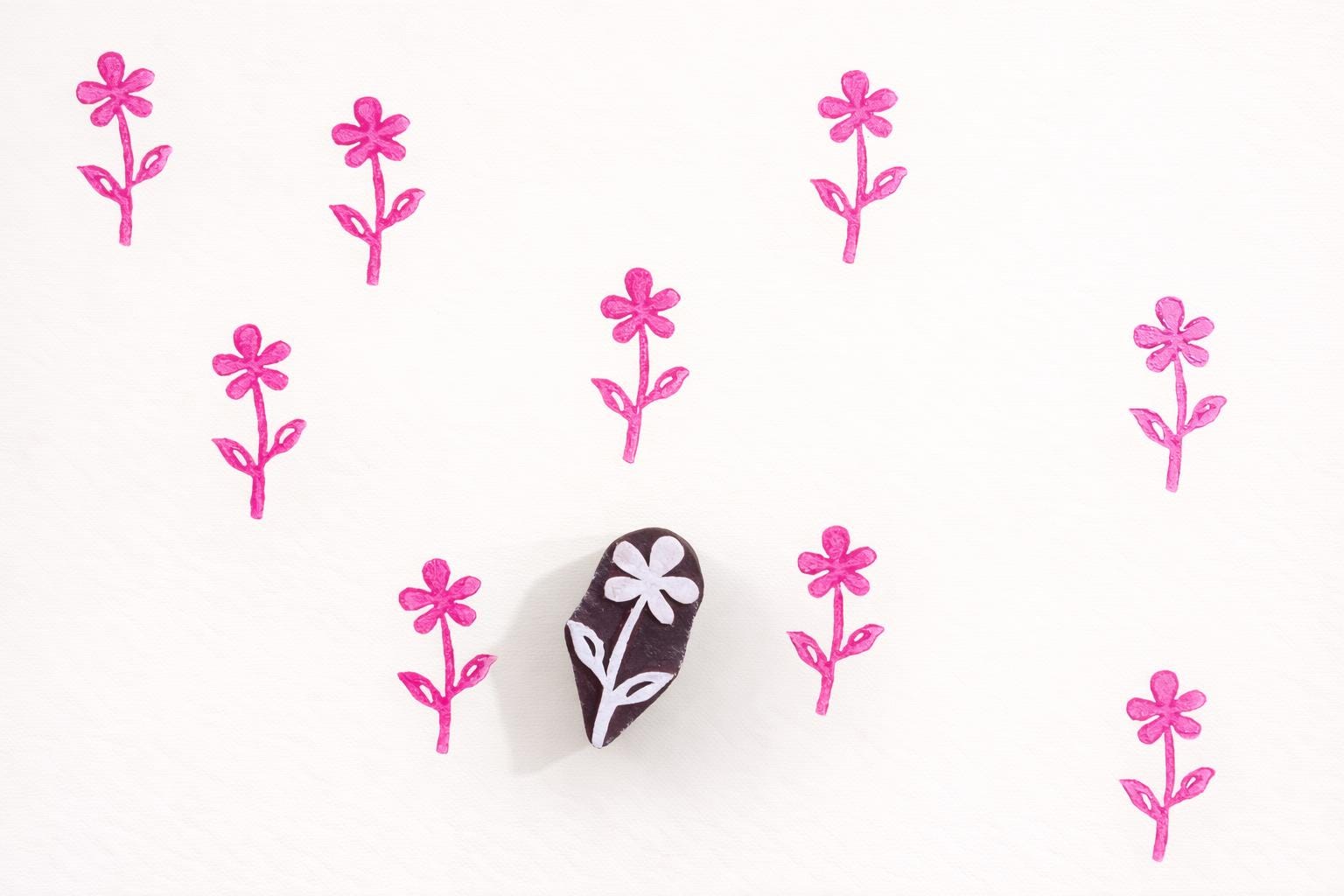 Small hand carved wooden flower block printing stamp creating repeating pink floral pattern on white background.