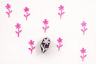 Small hand carved wooden flower block printing stamp creating repeating pink floral pattern on white background.