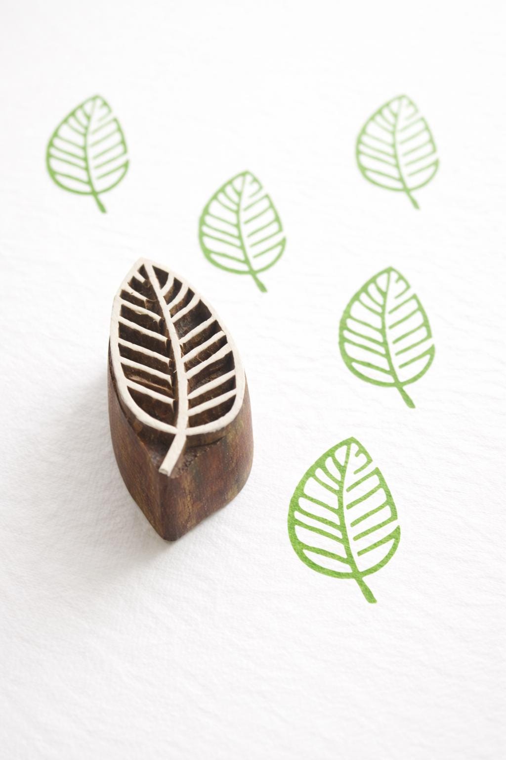 Hand carved Indian wooden printing block with a leaf design shown on white fabric with repeated green leaf prints.