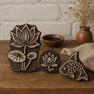 Set of hand carved Indian wooden printing blocks featuring lotus flower and fish designs displayed on a wooden surface.