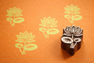 Hand carved Indian wooden printing block with a detailed lotus flower design shown on orange paper with repeated lotus prints.