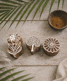 Set of three hand carved wooden block printing stamps featuring large botanical flower, tree of life, and round mandala floral design on rustic wooden surface.