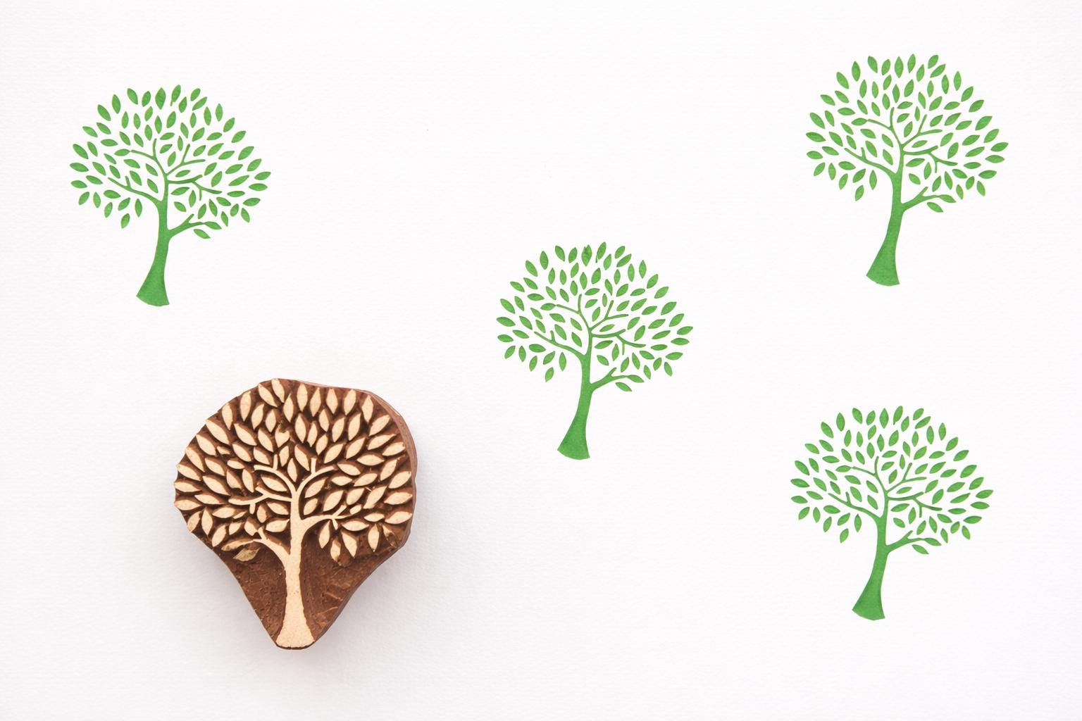 Hand carved wooden Tree of Life block printing stamp creating repeating green tree pattern on white background.