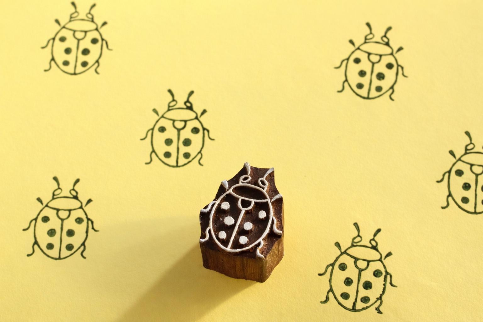 Hand carved ladybug wooden printing block with repeated ladybug pattern on yellow background