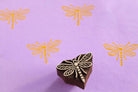 Hand carved dragonfly wooden printing block with repeated dragonfly prints on soft purple paper