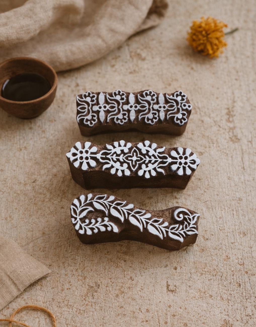 Hand carved wooden floral border block printing stamp creating vertical repeating pattern in multiple colors on white background.